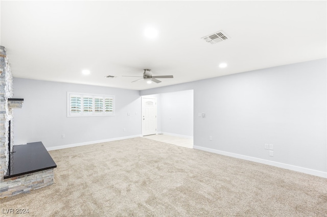 unfurnished living room with a stone fireplace, ceiling fan, and light colored carpet