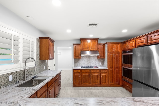 kitchen with light stone countertops, tasteful backsplash, stainless steel appliances, sink, and light hardwood / wood-style flooring