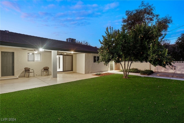 back house at dusk with ceiling fan, a patio area, and a yard