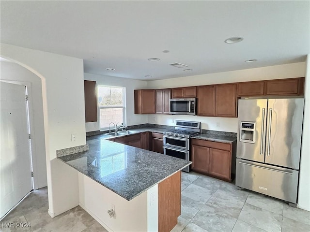 kitchen with kitchen peninsula, sink, dark stone countertops, and stainless steel appliances