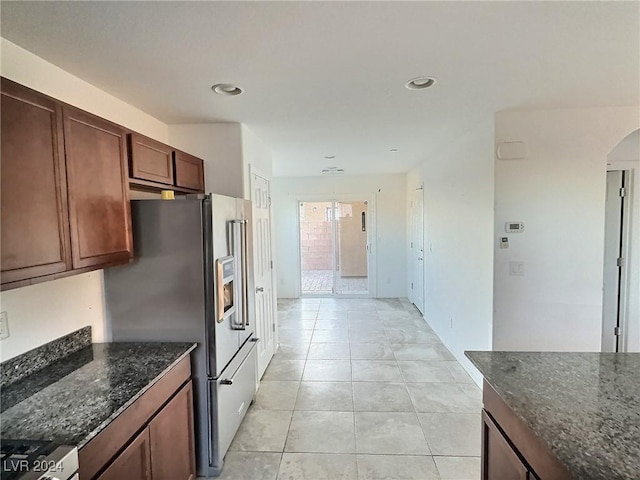 kitchen with dark stone countertops, high end refrigerator, light tile patterned floors, and range