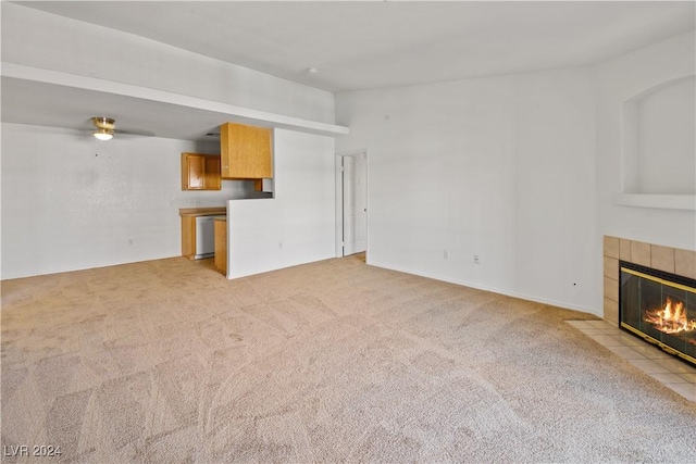 unfurnished living room with a tiled fireplace, light carpet, and ceiling fan