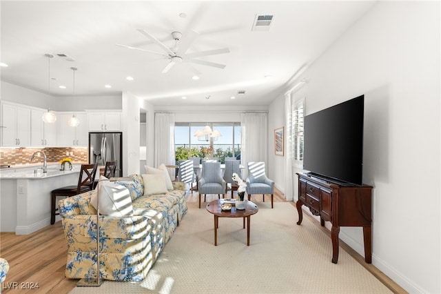 living room with ceiling fan with notable chandelier and light hardwood / wood-style flooring