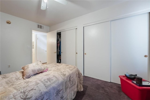 bedroom with ceiling fan, dark carpet, and multiple closets