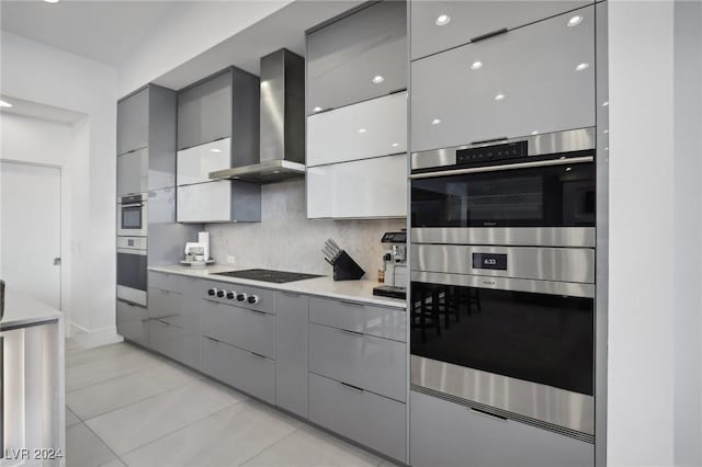 kitchen featuring tasteful backsplash, stainless steel double oven, wall chimney range hood, gas cooktop, and gray cabinets