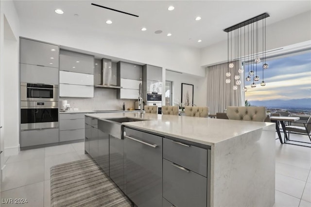 kitchen featuring a large island with sink, decorative light fixtures, wall chimney range hood, tasteful backsplash, and gray cabinets