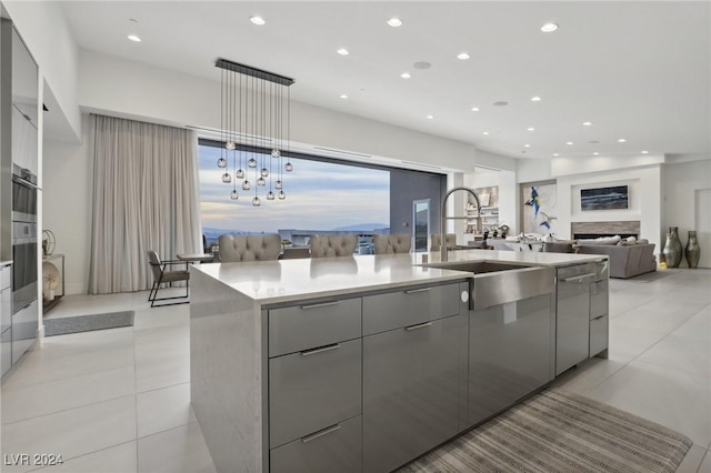 kitchen with appliances with stainless steel finishes, sink, decorative light fixtures, gray cabinetry, and a kitchen island with sink