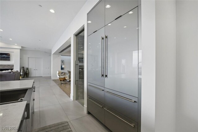 kitchen with gray cabinetry, light stone counters, a fireplace, light tile patterned flooring, and lofted ceiling