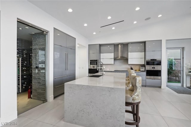 kitchen with wall chimney range hood, a kitchen bar, gray cabinetry, and lofted ceiling