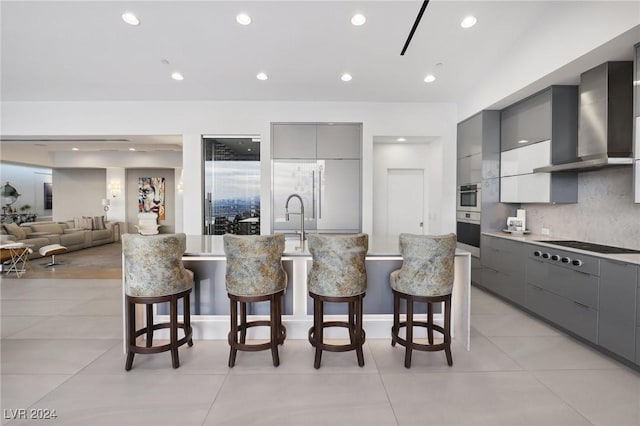 kitchen with wall chimney exhaust hood, appliances with stainless steel finishes, a breakfast bar area, and gray cabinetry