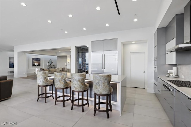 kitchen with a kitchen bar, appliances with stainless steel finishes, gray cabinetry, and wall chimney exhaust hood