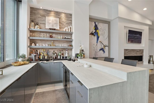 bar featuring light tile patterned floors, a fireplace, gray cabinetry, and lofted ceiling