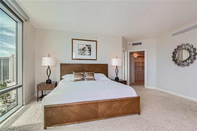 bedroom featuring a walk in closet, a closet, light colored carpet, and multiple windows