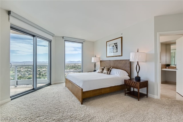 bedroom with a mountain view, light colored carpet, connected bathroom, and access to outside