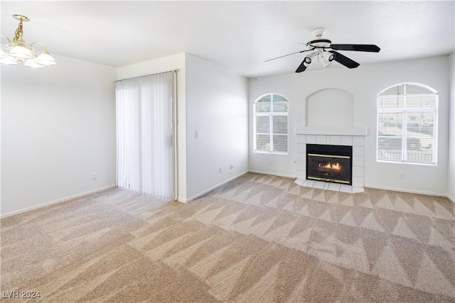 unfurnished living room featuring ceiling fan with notable chandelier, light colored carpet, and a tiled fireplace