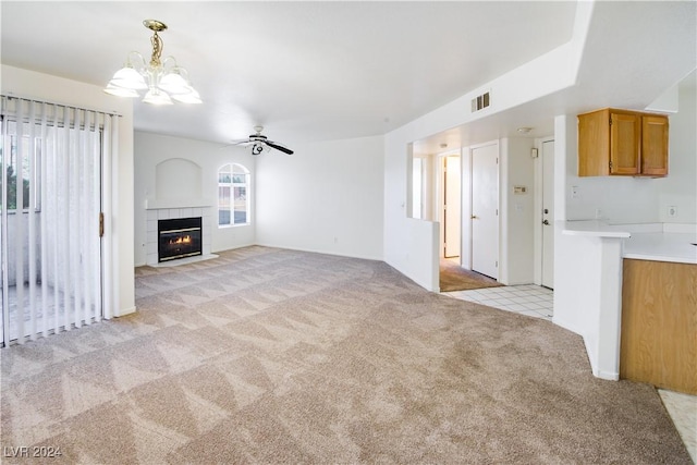 unfurnished living room featuring ceiling fan with notable chandelier, light colored carpet, and a tile fireplace