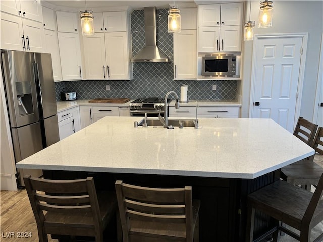 kitchen featuring stainless steel appliances, wall chimney range hood, an island with sink, pendant lighting, and a kitchen bar