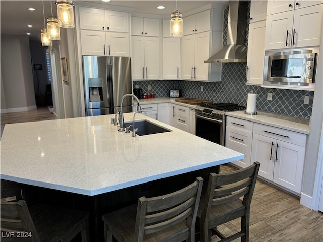 kitchen featuring a center island with sink, a kitchen breakfast bar, wall chimney range hood, and appliances with stainless steel finishes