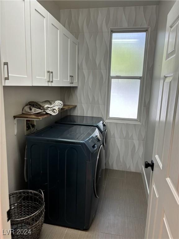 clothes washing area featuring cabinets, light tile patterned floors, washer and clothes dryer, and tile walls