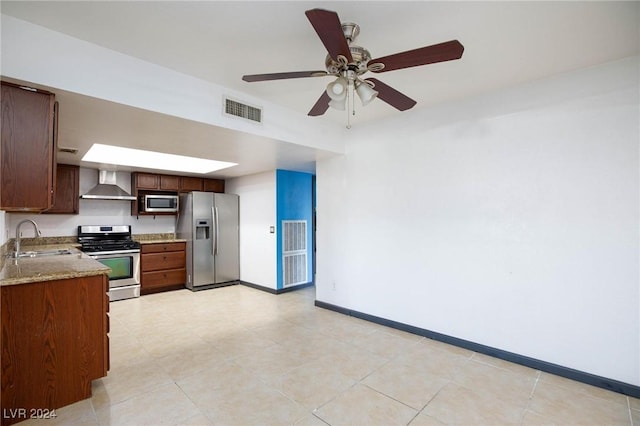 kitchen with ceiling fan, sink, wall chimney exhaust hood, stainless steel appliances, and light stone counters