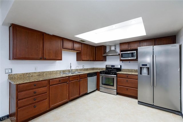 kitchen featuring light stone countertops, a skylight, stainless steel appliances, sink, and wall chimney range hood