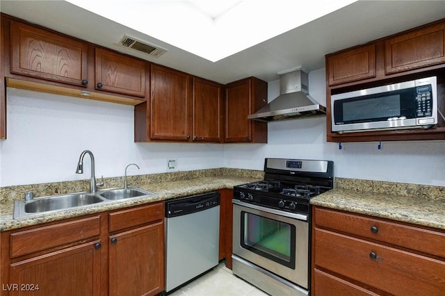 kitchen with light stone counters, stainless steel appliances, sink, wall chimney range hood, and light tile patterned floors