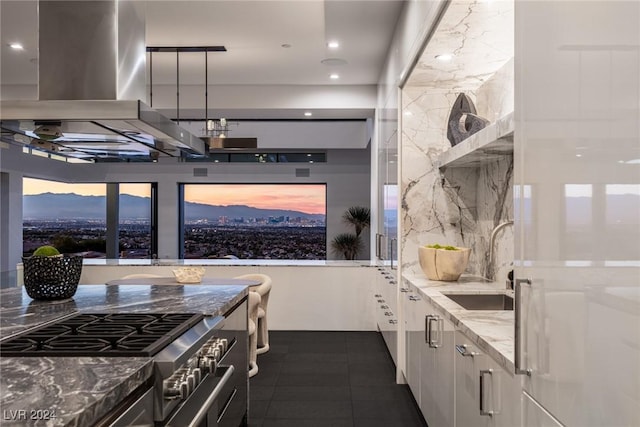 kitchen with dark stone counters, wall chimney exhaust hood, high end stainless steel range oven, sink, and hanging light fixtures