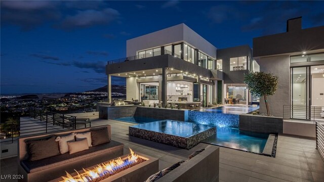 pool at twilight featuring pool water feature, an outdoor living space with a fire pit, and a patio