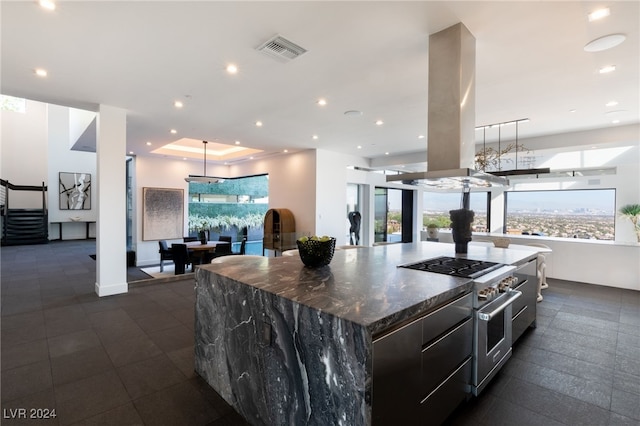 kitchen with island exhaust hood, dark stone counters, high end stove, hanging light fixtures, and a large island