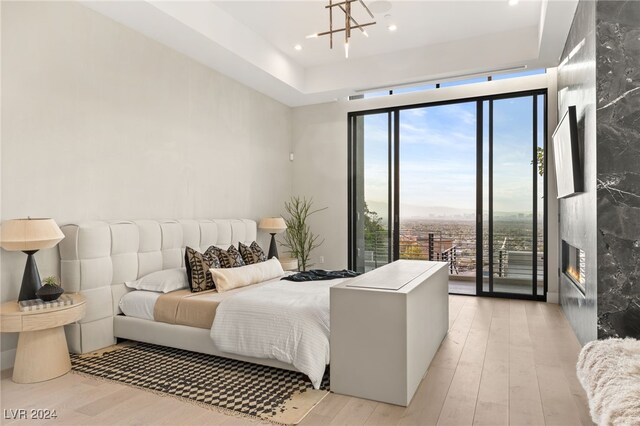 bedroom with access to exterior, a high end fireplace, floor to ceiling windows, an inviting chandelier, and light hardwood / wood-style flooring