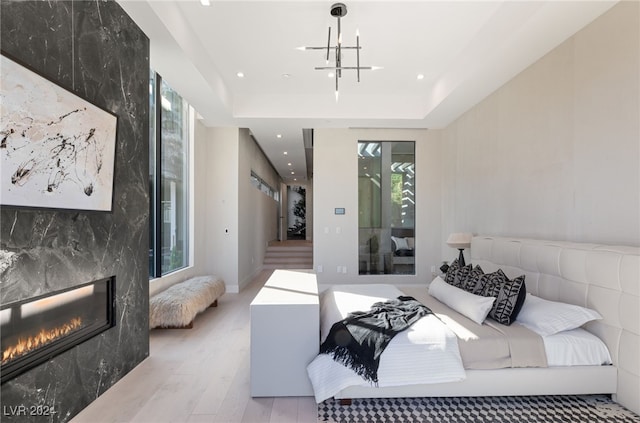 bedroom featuring a high end fireplace, light wood-type flooring, a chandelier, and multiple windows