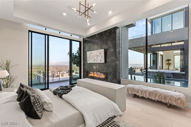 bedroom featuring light hardwood / wood-style floors, access to outside, a high end fireplace, and an inviting chandelier