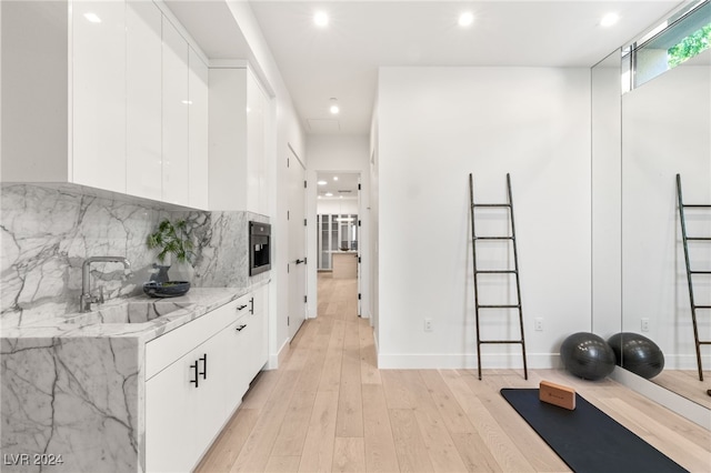 interior space featuring white cabinets, light stone countertops, sink, and light hardwood / wood-style flooring