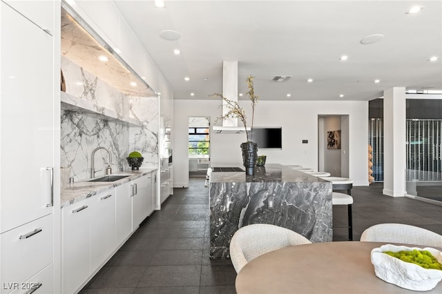 kitchen featuring backsplash, sink, light stone countertops, white cabinetry, and a breakfast bar area