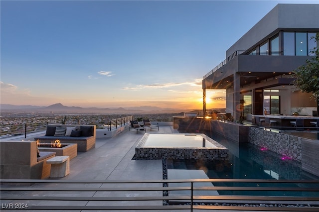 pool at dusk with a mountain view, a hot tub, and an outdoor fire pit