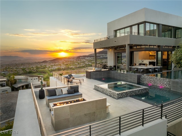 patio terrace at dusk with an in ground hot tub, outdoor lounge area, a balcony, and a mountain view