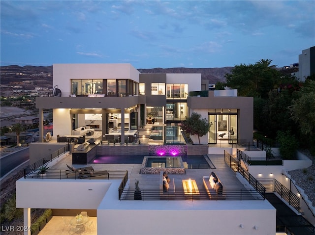 back house at dusk featuring a mountain view, a swimming pool with hot tub, and a patio