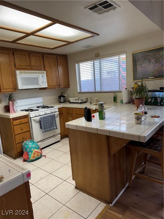4764 Anchorage St, Las Vegas, NV 89147 - kitchen featuring white appliances, brown cabinets, a peninsula, and tile countertops