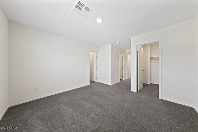 unfurnished bedroom with dark colored carpet, a spacious closet, and a closet