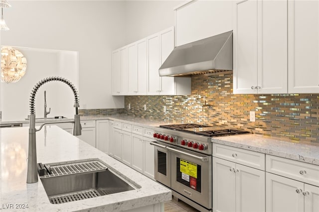 kitchen with wall chimney exhaust hood, double oven range, white cabinetry, and decorative backsplash