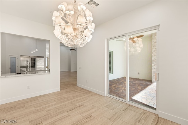 unfurnished dining area featuring ceiling fan with notable chandelier, light hardwood / wood-style floors, and sink