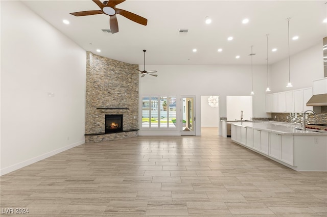 unfurnished living room with a towering ceiling, ceiling fan, sink, light hardwood / wood-style flooring, and a stone fireplace