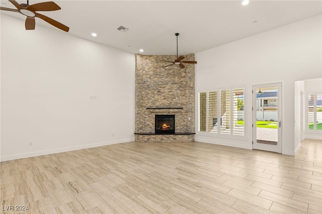 unfurnished living room with a towering ceiling, a fireplace, a wealth of natural light, and light hardwood / wood-style flooring