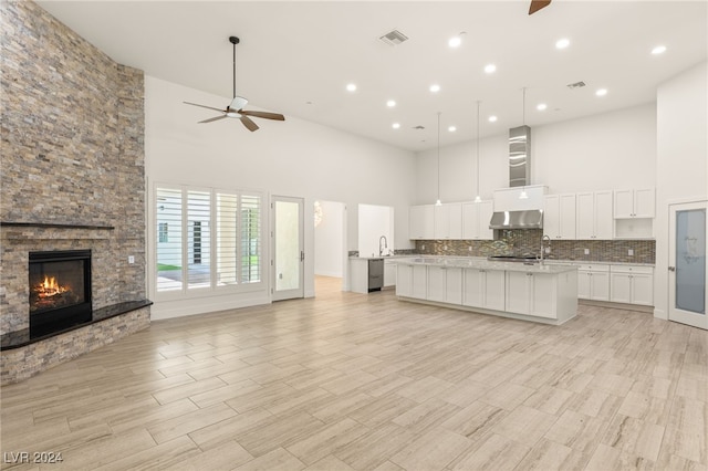 kitchen featuring a kitchen island with sink, exhaust hood, white cabinets, a towering ceiling, and a fireplace