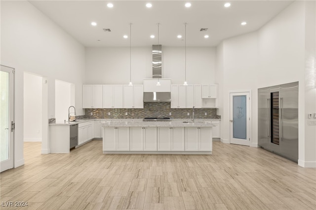 kitchen with light hardwood / wood-style floors, a towering ceiling, white cabinetry, and exhaust hood