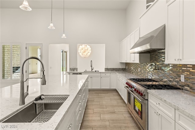 kitchen with light stone counters, sink, wall chimney exhaust hood, and range with two ovens