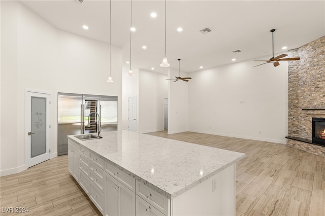 kitchen with white cabinets, a stone fireplace, light hardwood / wood-style flooring, an island with sink, and decorative light fixtures