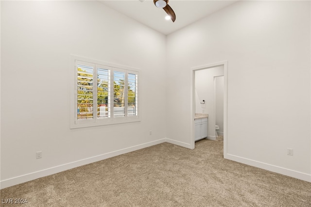 unfurnished bedroom featuring connected bathroom, ceiling fan, a towering ceiling, and light carpet