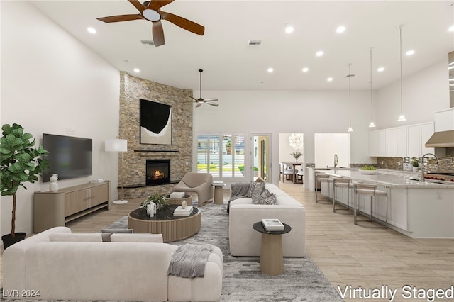 living room with a stone fireplace, ceiling fan, sink, and a high ceiling