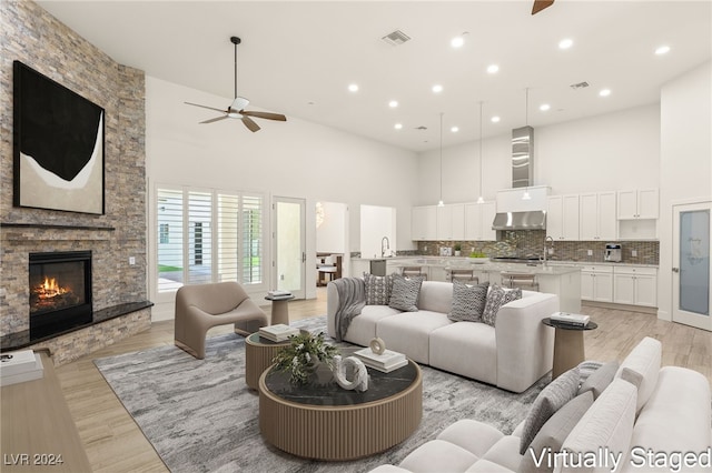 living room with a stone fireplace, ceiling fan, a towering ceiling, and light hardwood / wood-style floors